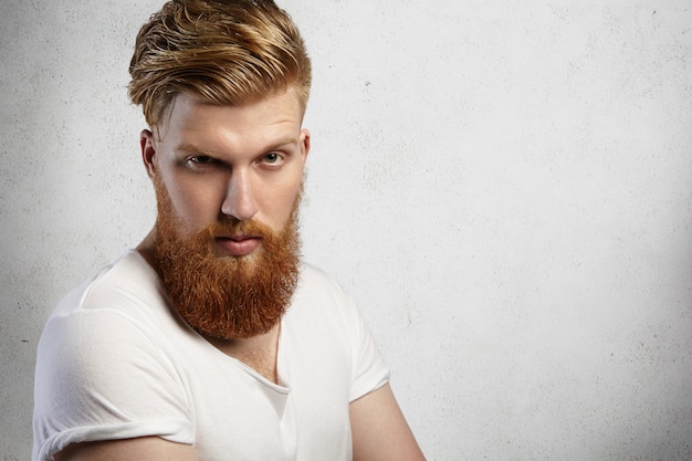Free photo human face expressions and emotions. headshot of young model with thick beard posing with angry and unfriendly look.