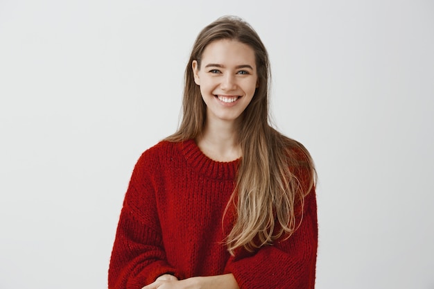 Free photo indoor shot of charming friendly-looking european woman in stylish loose sweater, talking casually with coworker during break at work, smiling broadly, being charmed and excited with conversation