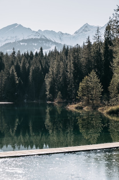 Бесплатное фото Озеро, окруженное горами, покрытыми снегом, и лесом с деревьями, отражающимися в воде.