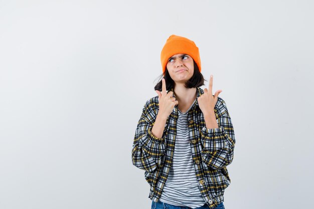 Free photo little woman in t-shirt jacket beanie pointing up looking hesitant