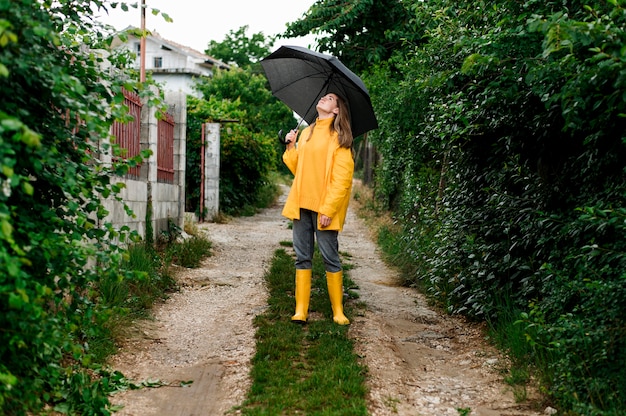 Free photo long shot woman in rain clothes holding an umbrella