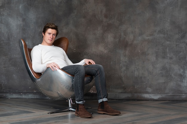 Free photo long shot young man sitting on leather armchair
