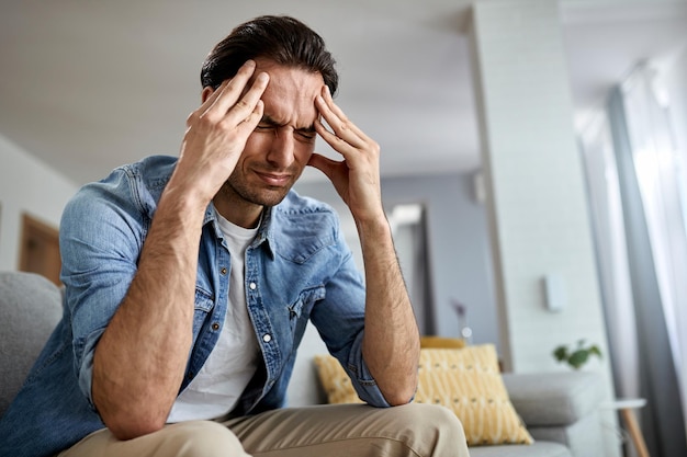 Free photo low angle view of distraught man holding his head in pain while sitting in the living room