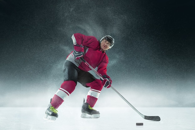 Бесплатное фото Хоккеист мужского пола с клюшкой на ледовой площадке и темной стене