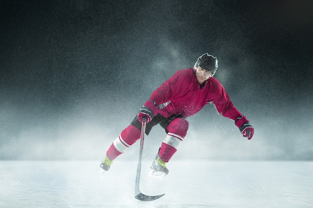 Бесплатное фото Хоккеист мужского пола с клюшкой на ледовой площадке и темной стене