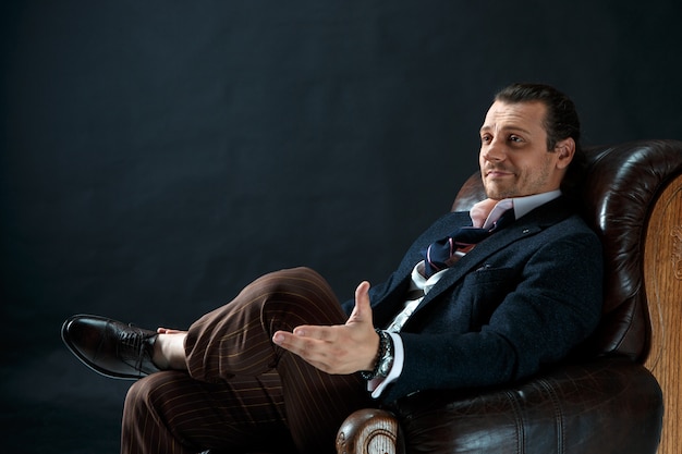 The mature stylish man in a suit on a gray studio. Businessman sitting on an armchair