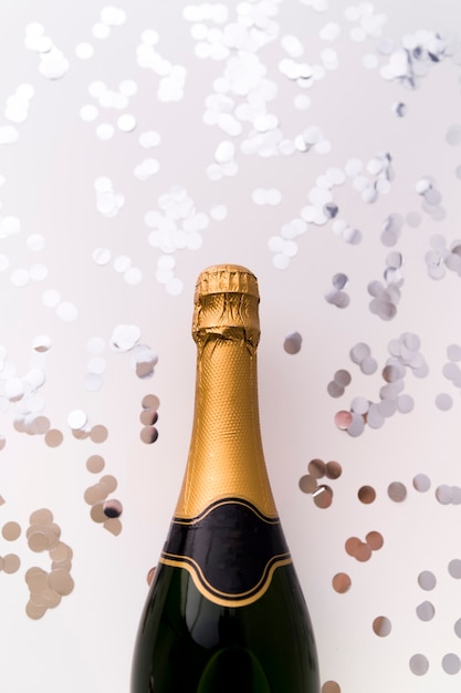 Бесплатное фото Новая бутылка шампанского и серебряное круглое конфетти на белом фоне