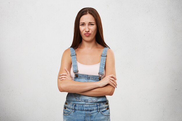 Free photo picture of attractive young caucasian female with dark straight hair posing, keeping arms folded, having offended look, pouting lips, showing her dislike, negative attitude and rigidity