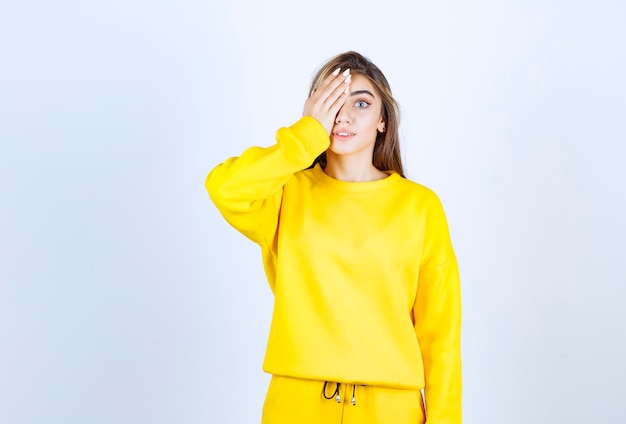 Free photo portrait of young woman in yellow outfit standing and covering her eye