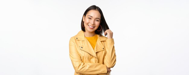 Foto gratuita ritratto di donna asiatica in giacca gialla sorridente e guardando felice in piedi su sfondo bianco copia spazio