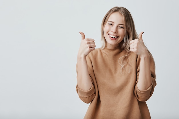 Free photo portrait of fair-haired beautiful female woman with broad smile and thumbs up