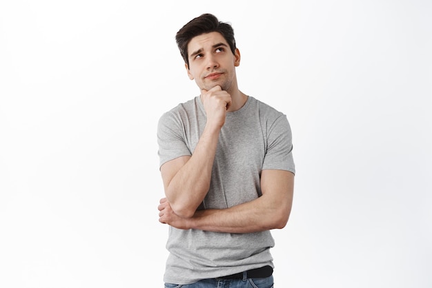 Free photo portrait of handsome man in deep thoughts looking aside touching chin and thinking looking aside imaging something standing over white background