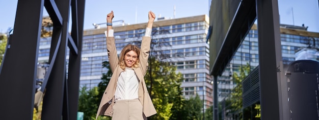 Free photo portrait of happy young businesswoman lift hands up does fist pump celebrates victory wins smth