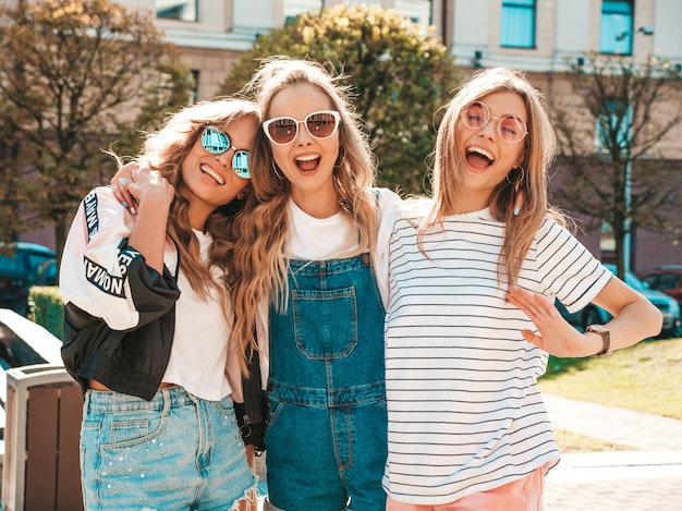 Бесплатное фото Портрет трех молодых красивых улыбающихся хипстерских девочек в модной летней одежде. сексуальные беззаботные женщины позируют на улице. позитивные модели веселятся в солнечных очках. обнимаются
