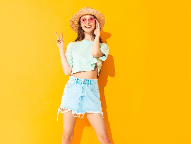 Бесплатное фото Портрет молодой красивой улыбающейся женщины в модной летней джинсовой юбке беззаботная женщина позирует возле желтой стены в студии позитивная модель веселится в помещении веселая и счастливая в шляпе