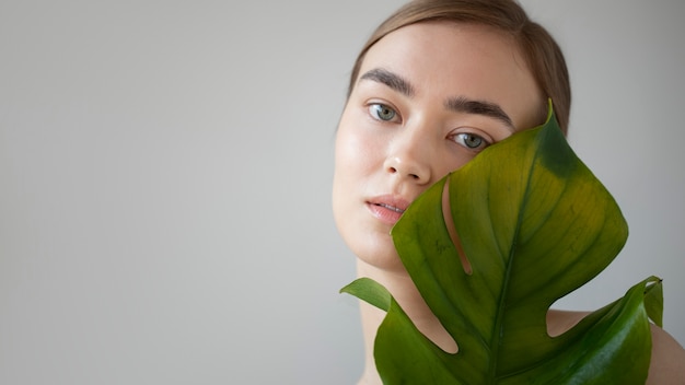 Бесплатное фото Портрет красивой женщины с чистой кожей, позирующей с листьями растения-монстра