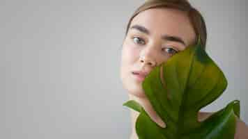 Бесплатное фото Портрет красивой женщины с чистой кожей, позирующей с листьями растения-монстра
