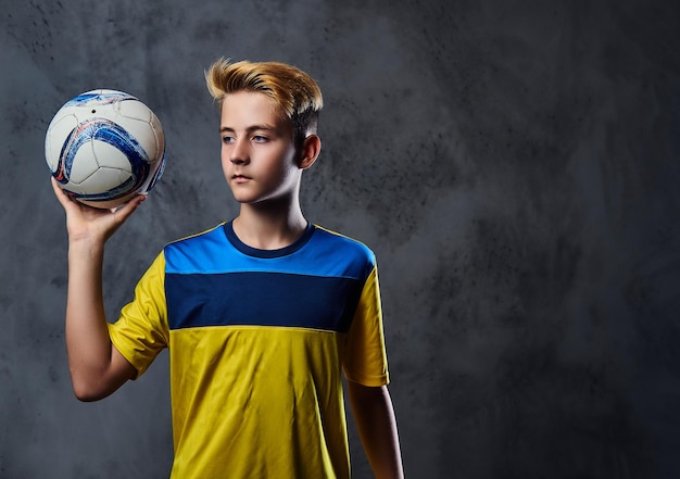 Бесплатное фото Портрет белокурого подростка, футболиста, одетого в желтую форму, держит мяч.