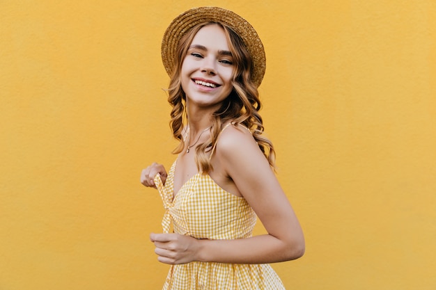 Бесплатное фото Портрет модной курчавой женщины улыбается. крытый выстрел милой женской модели в ретро платье и шляпе.