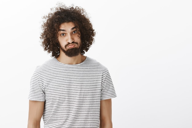 Free photo portrait of plyaful carefree attractive male model with beard and curly hair, sticking out tongue and pouting, making funny faces