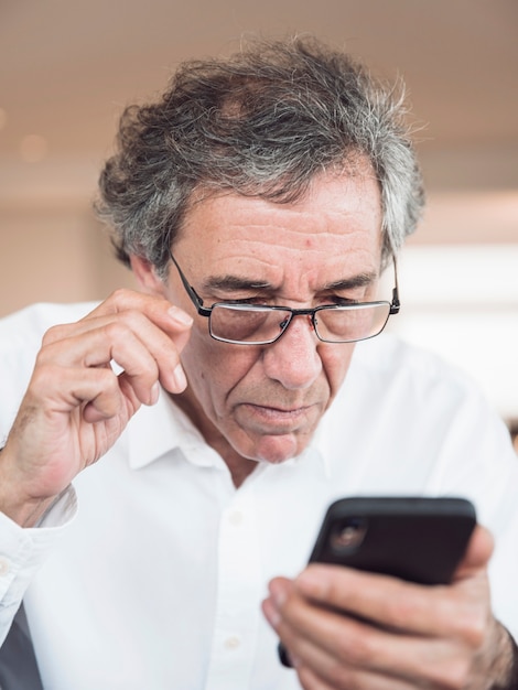 Free photo portrait of senior man wearing eyeglasses looking at mobile phone