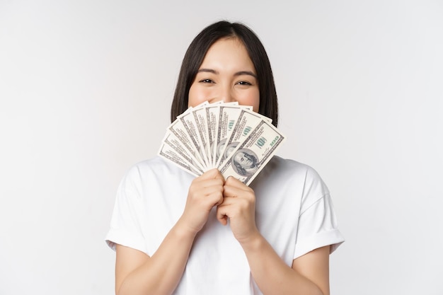 Портрет улыбающейся азиатской женщины, держащей доллары, концепция микрокредитного финансирования и наличных денег, стоящих на белом фоне