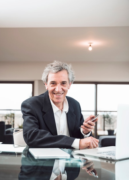 Free photo portrait of smiling senior man with digital tablet and laptop on glass reflective desk