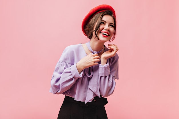 Бесплатное фото Позитивная женщина в красном берете и сиреневой блузке смеется на розовом фоне.