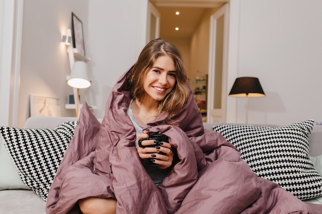 Бесплатное фото Довольная европейская женщина пьет чай на диване в холодный день