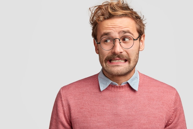 Free photo puzzled attractive bearded emotive man wonk in spectacles, looks with worried embarrassed expression aside
