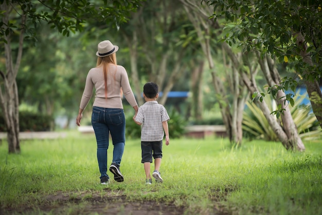 무료 사진 어머니와 아들이 손을 잡고 집 정원에서 함께 걷는 후면보기.