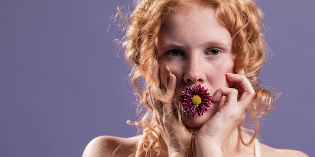 Redhead woman posing with a chrysanthemum on her mouth and copy space