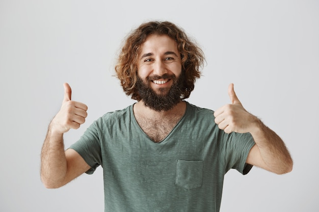 Free photo satisfied bearded guy showing thumbs-up in approval, smiling happy