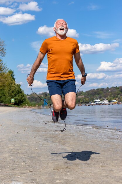 Старший мужчина прыгает через скакалку, тренируется на пляже.