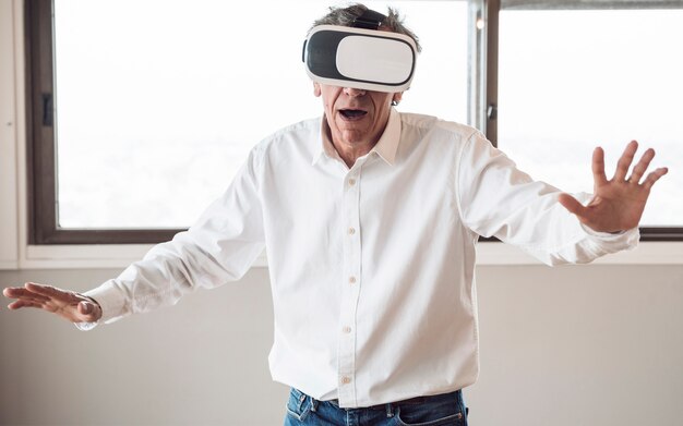 Free photo senior man in white shirt using a virtual reality headset in the room