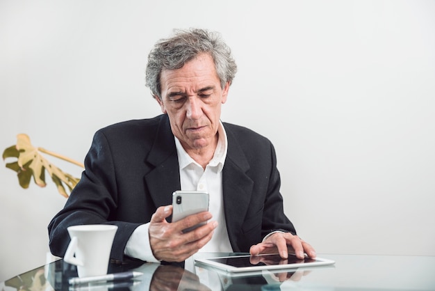 Free photo senior man with digital tablet looking at mobile phone
