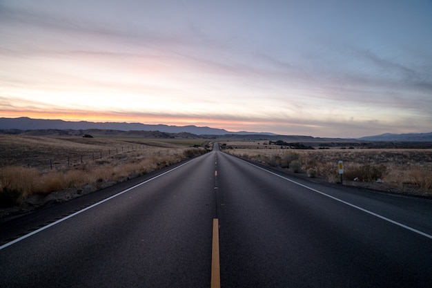 Free photo shot of a highway road surrounded by dried grass fields under a sky during sunset