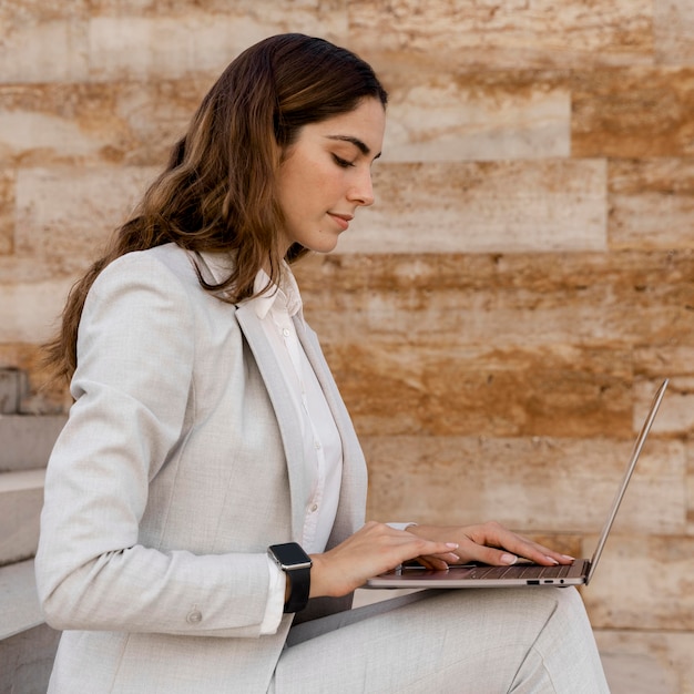 Foto gratuita vista laterale della donna di affari elegante con smartwatch che lavora al computer portatile all'aperto