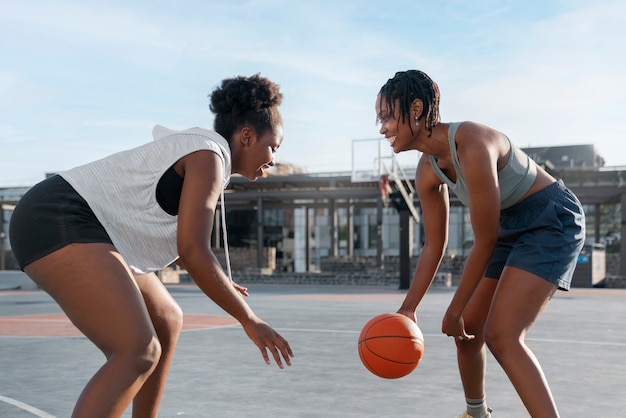 Бесплатное фото Вид сбоку подруги, играющие в баскетбол