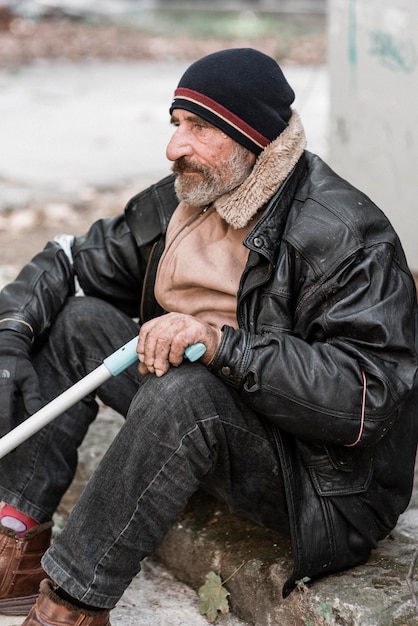 Бездомный мужчина держит трость, вид сбоку