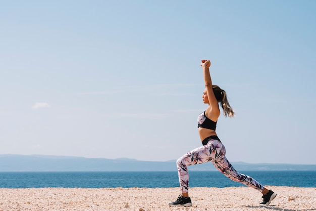 Бесплатное фото Вид сбоку молодой женщины, растяжения упражнения рядом с пляжем