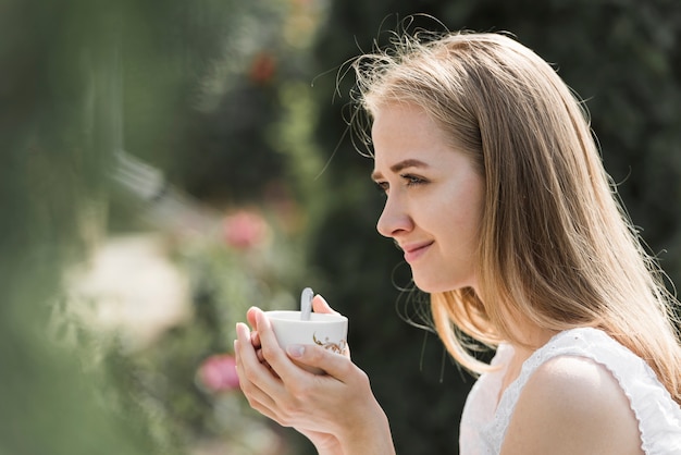 Бесплатное фото Вид сбоку молодой женщины, держащей чашку кофе в двух руках