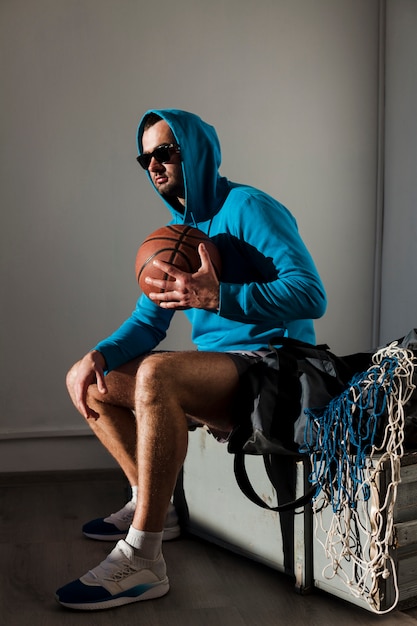 Бесплатное фото Вид сбоку баскетболист, позирует в балахон с мячом