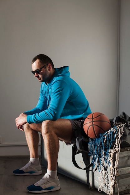 Бесплатное фото Вид сбоку человека в балахон и солнцезащитные очки с баскетболом рядом с ним
