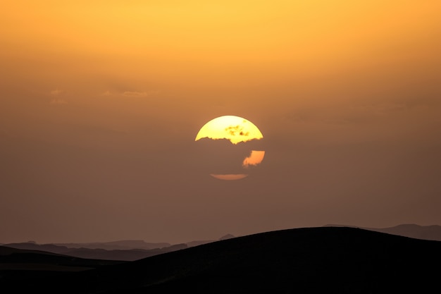 Бесплатное фото Силуэт песчаных дюн с солнцем за облаком