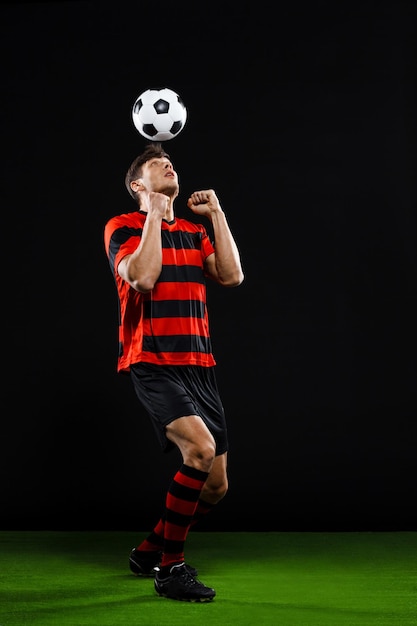 Бесплатное фото Футболист пинает мяч на черном фоне