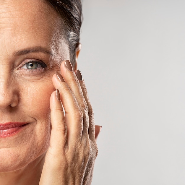 Free photo smiley mature woman with make-up on posing with hand on face