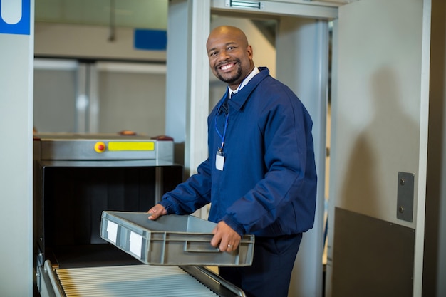 Free photo smiling airport security officer holding a crate near conveyor belt