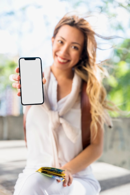 Бесплатное фото Усмехаясь белокурая молодая женщина держа карту в руке показывая передвижной пустой белый экран