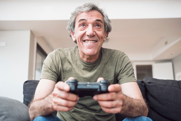 Free photo smiling senior man sitting on sofa enjoying playing the video game